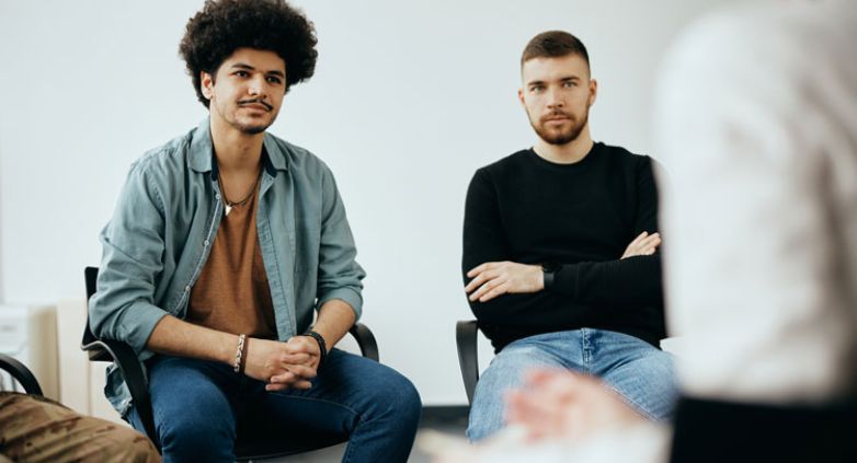 A group of people seated in a circle engage in a conversation, reflecting emotional distress related to drug addiction's impact on families.