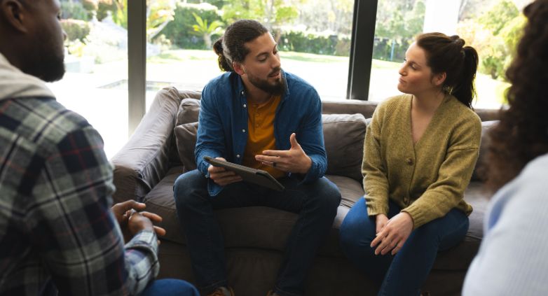 A group of individuals seated on a couch engaged in conversation, reflecting the impact of drug addiction on family dynamics.