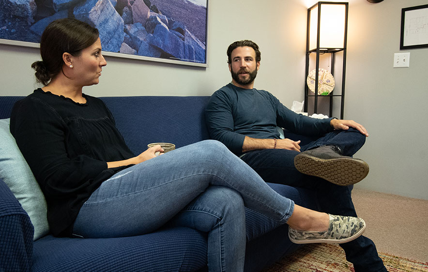 A man and woman on a couch in an office setting, engaged in a conversation about Addiction Recovery Services in Deep River.