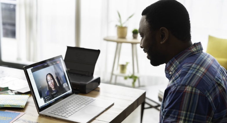 A man seated at a desk with a laptop, engaging with a woman on the screen about the effectiveness of virtual recovery programs.