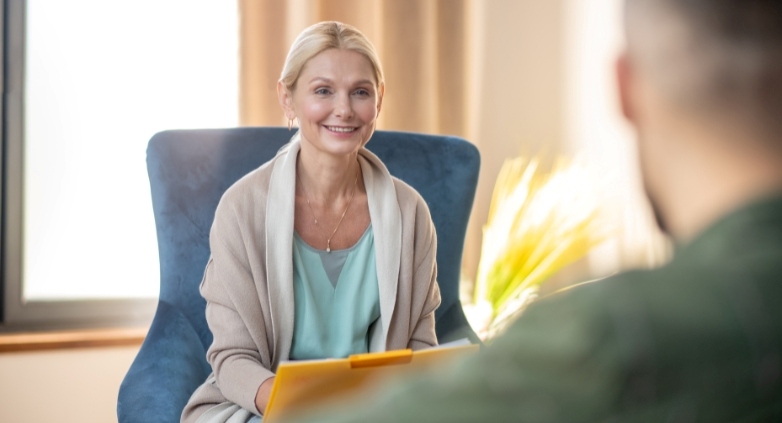 A woman seated in a chair engages in conversation with a man, discussing ways to support a family member struggling with addiction.