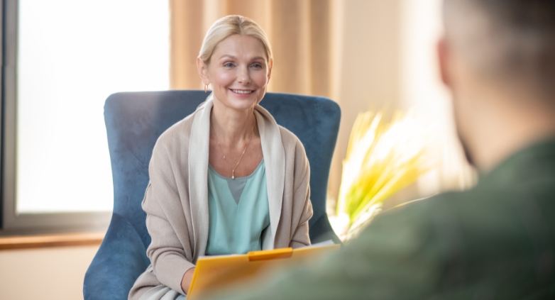 A woman seated in a chair engages in conversation with a man, discussing ways to support a family member struggling with addiction.