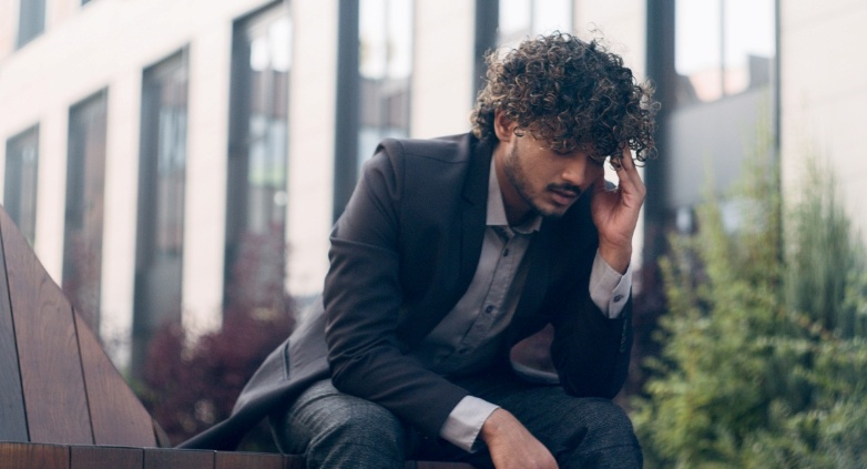 A man in a suit sits on a bench, reflecting on the signs of a potential drinking problem.