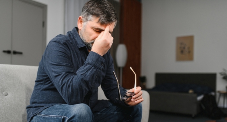 A man on a couch, head in hands, contemplating his relationship with alcohol and questioning his drinking behavior.
