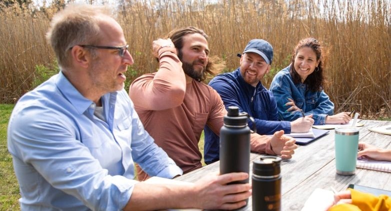 Several individuals seated at a picnic table, engaged in conversation about family support for an alcoholic son.