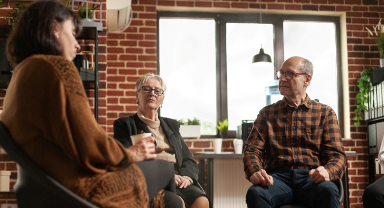 Three individuals in chairs conversing about the challenges faced by parents of an alcoholic son and their emotional struggles.