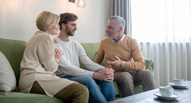 A man and woman are seated on a couch, talking to a man about the challenges of supporting their son with alcoholism.