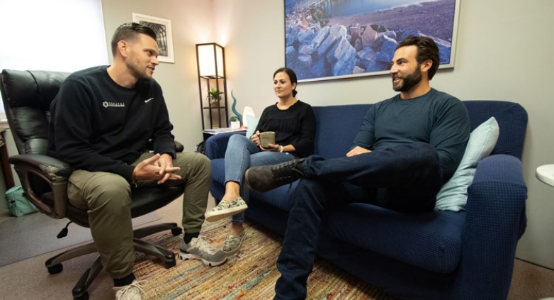 Three people on a couch in an office setting, engaged in a group therapy session for drug addiction support.