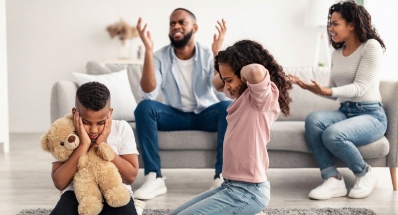 A family sits on the floor with a teddy bear, highlighting the impact of living with an alcoholic on children.