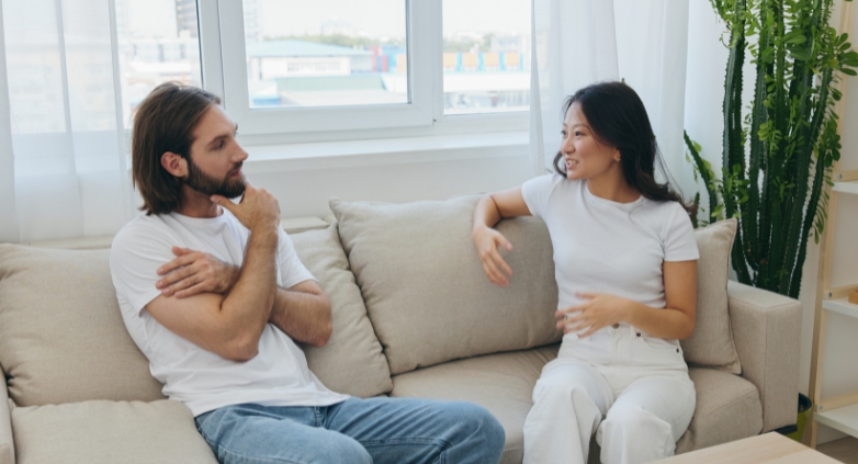 A man and woman converse on a couch, focusing on the topic of coping with an alcoholic spouse.