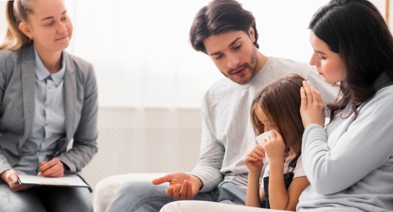 A therapist and parents with their child sits on a couch, reflecting the impact of addiction on trust and relationships.