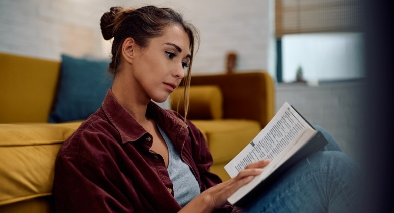 A woman reads a book on a couch, focusing on strategies for supporting an alcoholic daughter through education.