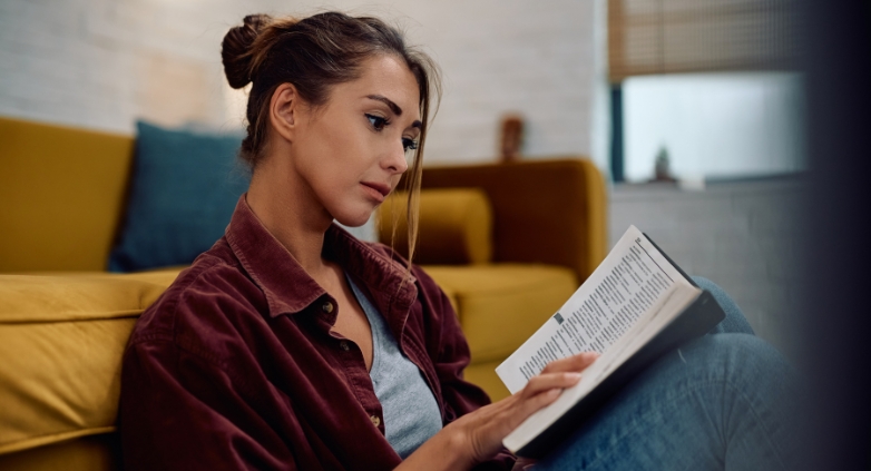 A woman reads a book on a couch, focusing on strategies for supporting an alcoholic daughter through education.