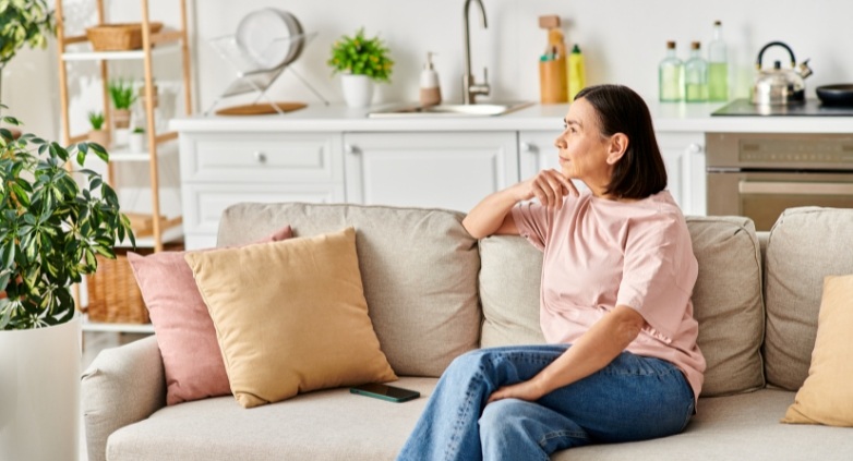 A woman sitting on a couch in a living room, reflecting on ways to support her alcoholic daughter.