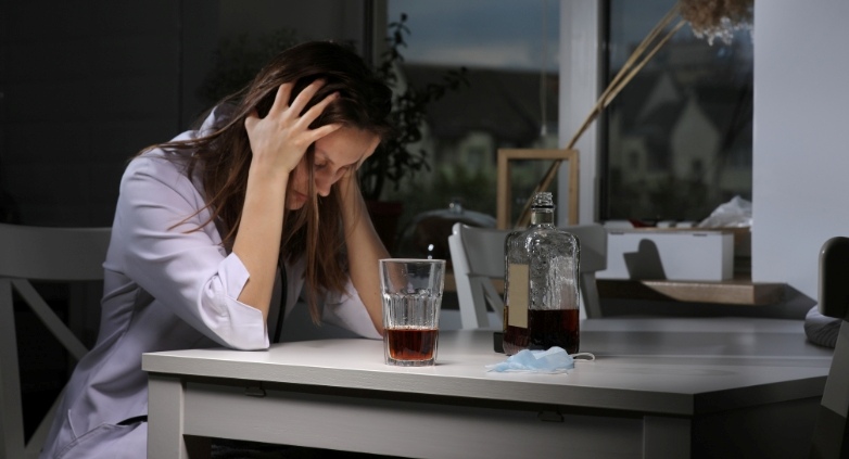 A woman at a table with a drink and a bottle of alcohol, symbolizing the challenges of addressing alcoholism in family.