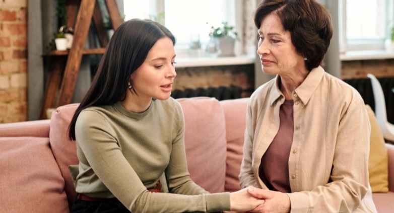 A daughter and her mother sitting on a couch, discussing signs of alcoholism and how to support a daughter in need.