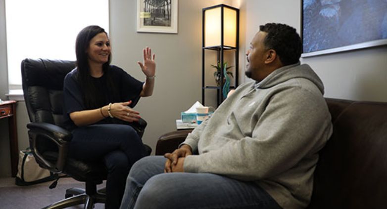 A man and woman sit in an office, engaged in a serious conversation about supporting an alcoholic family member.