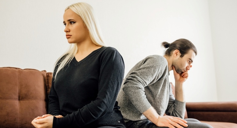 A man and woman are seated on a couch, contemplating the difficulties of living with an alcoholic spouse.