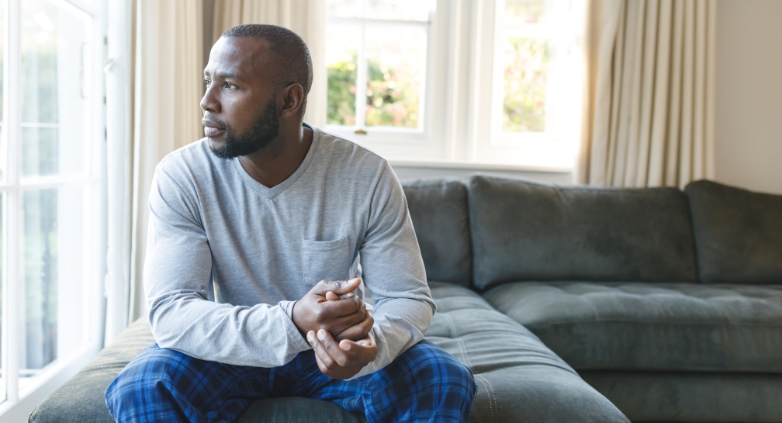 A man sits on a couch by a window, reflecting on the impact of addiction on families in recovery.