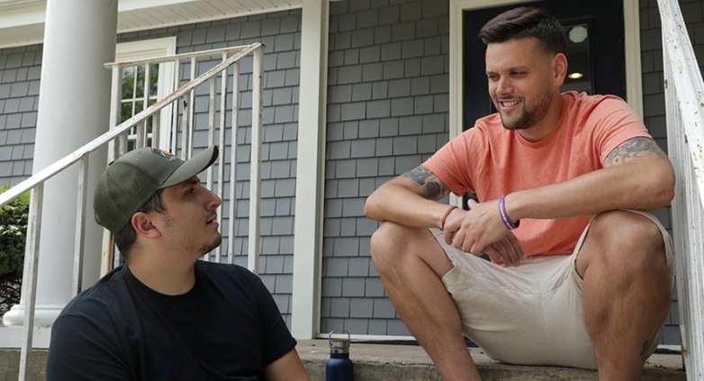 Two men on the steps of a house, showcasing on how to assist an addict without enabling their addiction.