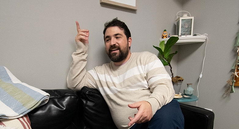A man seated on a couch, hands raised, illustrating the need for support in family addiction recovery discussions.