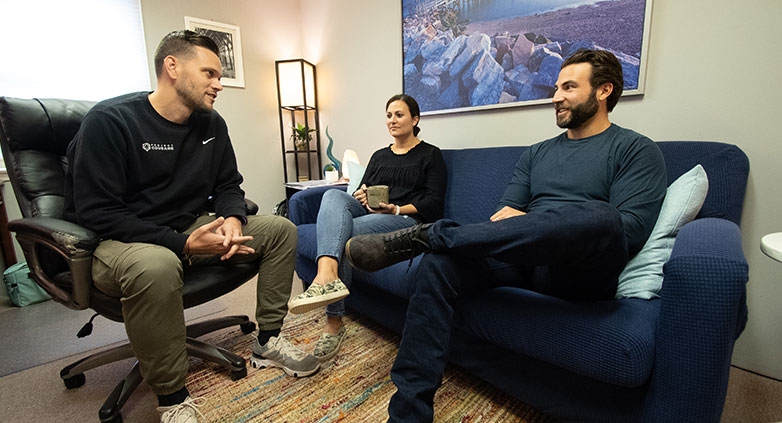 Three people on a couch in an office setting, engaged in a support group for families affected by addiction.
