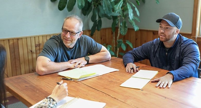 A group of people at a table with documents and a pen, engaged in a discussion about helping families with alcoholic parents.