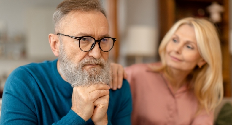 An older man wearing glasses and a woman are seated on a couch, focusing on how to identify signs of an alcoholic parent.