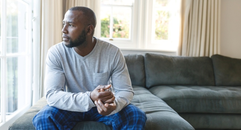 A man sits on a couch by a window, reflecting on physical boundaries in addiction recovery.