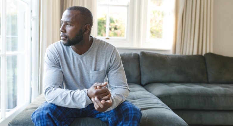 A man sits on a couch by a window, reflecting on physical boundaries in addiction recovery.