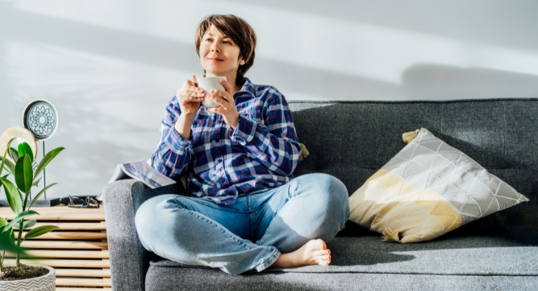 A woman on a couch enjoys a cup of coffee while considering the significance of boundaries in addiction recovery.