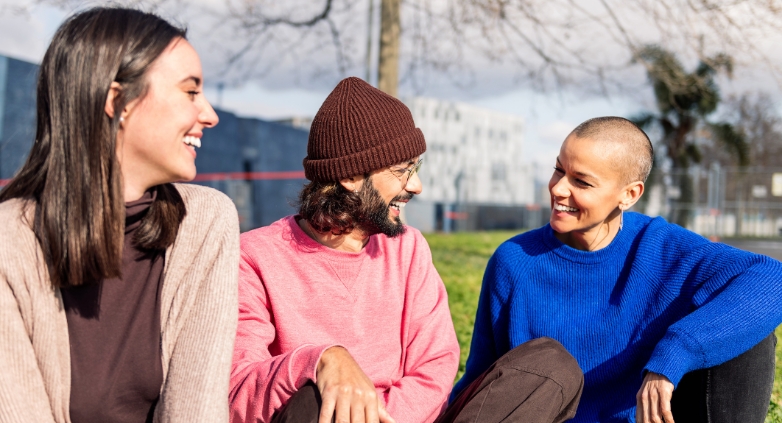 Three young adults chat on the grass, focusing on ways to foster a recovery-friendly atmosphere.