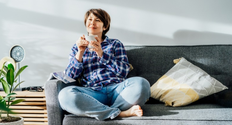 A woman on a couch enjoys a cup of coffee, symbolizing self-care in the journey of supporting sobriety.