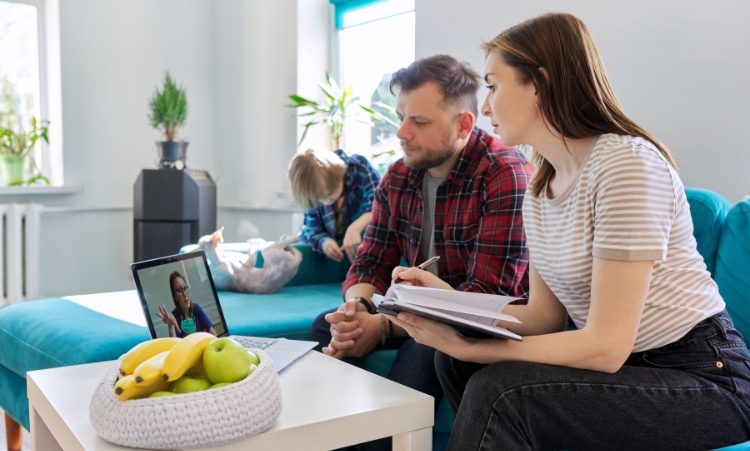 A man and woman are seated on a couch with a laptop, participating in virtual addiction treatment and family recovery support.