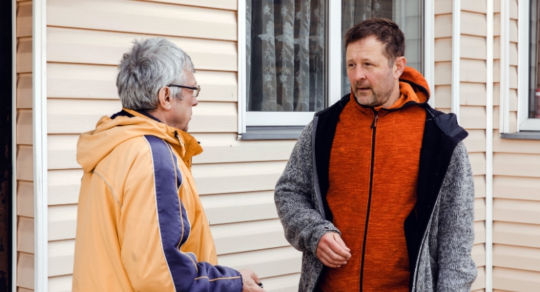 Two men talking outside a house, focusing on how to safely help an alcoholic father.