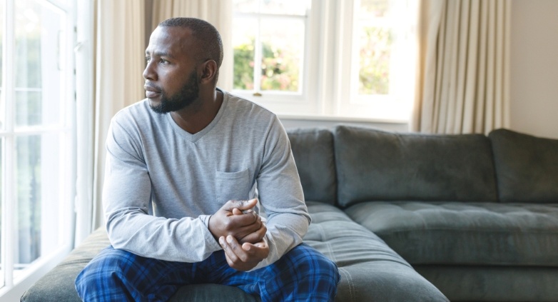 A man relaxes on a couch in front of a window, considering ways to assist an alcoholic father by recognizing key signs.