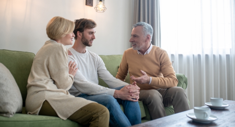 A family are seated on a couch, talking about their concerns regarding a loved one's drinking habits during the holidays.