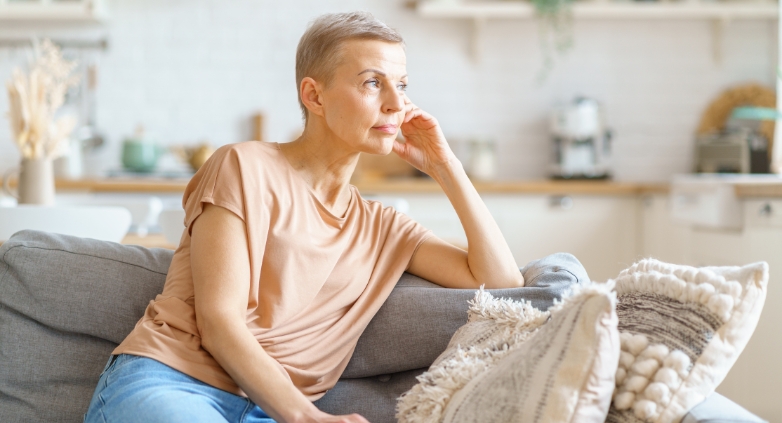 A woman sitting on a couch in her living room, reflecting on the challenges of helping an alcoholic mother.