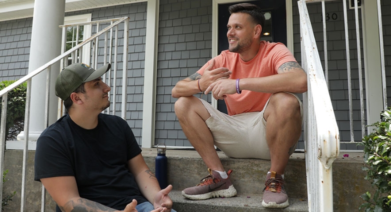 Two men seated on house steps, engaged in conversation about coping with sobriety during the holidays.