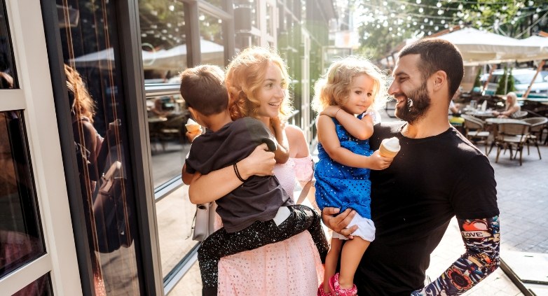 A man and woman stand outside, holding a child, symbolizing family dynamics affected by parental alcoholism.
