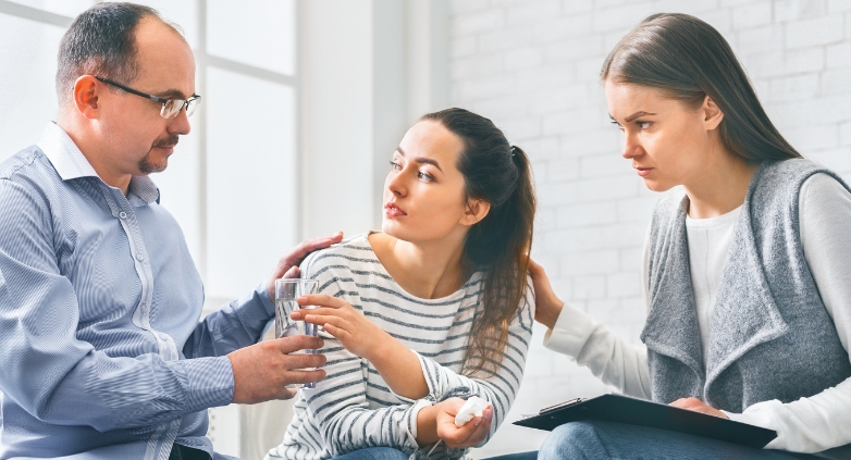 A man and woman talk, while another man watches, representing the challenges families face due to teenage drug addiction.