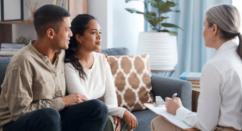 A couple engages in conversation with a therapist on a couch, addressing family challenges in addiction recovery support.