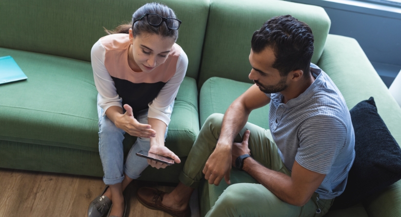 A man and woman seated on a couch look at a cell phone, exploring ways families can aid loved ones in addiction recovery.