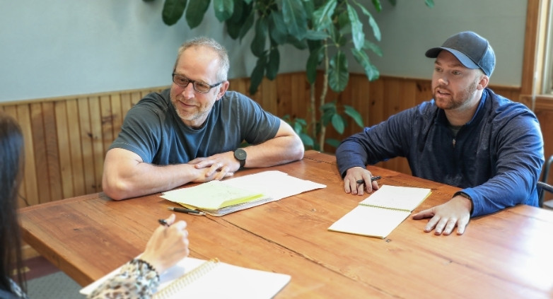 Two men at a table with papers and a pen, collaborating on family therapy models for addiction treatment.