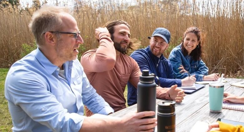 A diverse group of individuals at a table with water bottles, involved in a drug addiction support group discussion.