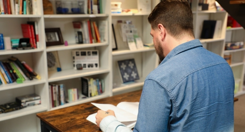 A man studies a book on addiction communication, surrounded by shelves filled with various books.