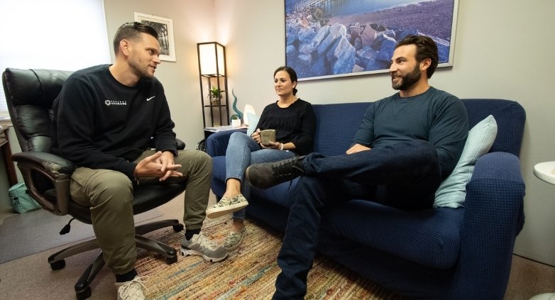 Three people sitting together on a couch in an office, focusing on professional resources for family addiction discussions.