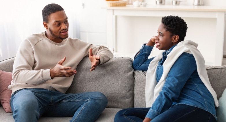 A couple on a couch, having a heartfelt discussion about navigating addiction and establishing healthy boundaries.