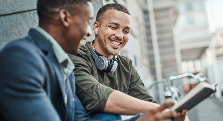 Two men seated on a bench, looking at a tablet, reviewing scripts for talking about addiction using the OARS method.