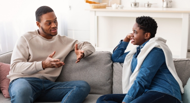 A couple on a couch, having a thoughtful discussion about how to assist a family member struggling with addiction.